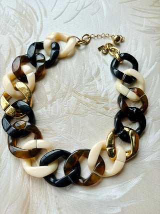 Necklace with black, white, and gold chain links on a textured beige background
