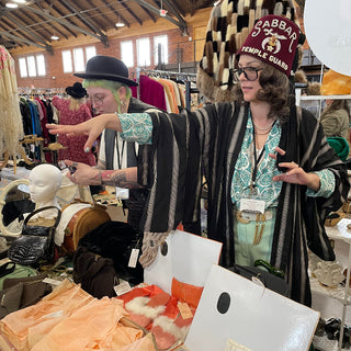 Person shopping in a store with various vintage clothing and accessories displayed.